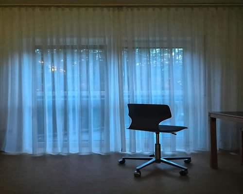 A home office desk positioned perpendicular to a large window with sheer curtains